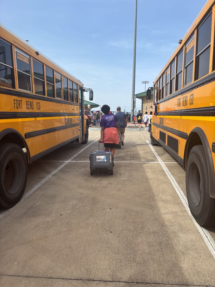 A person is pulling a suitcase between two school buses