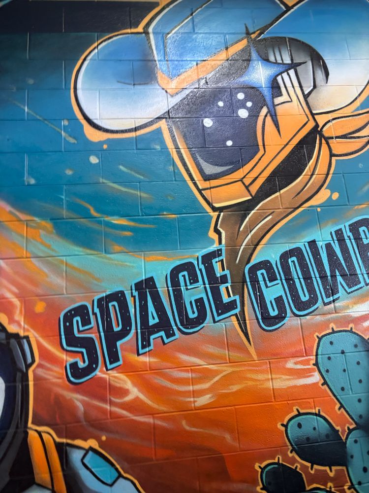 A mural on a brick wall that says space cow