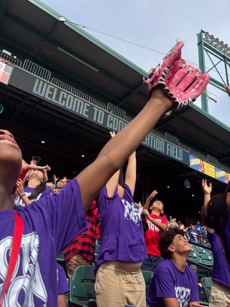A girl in a purple shirt is holding a baseball glove in the air