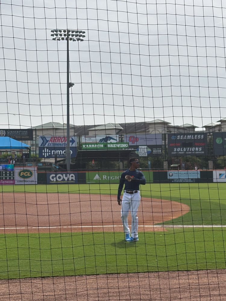 A man is standing on a baseball field behind a net