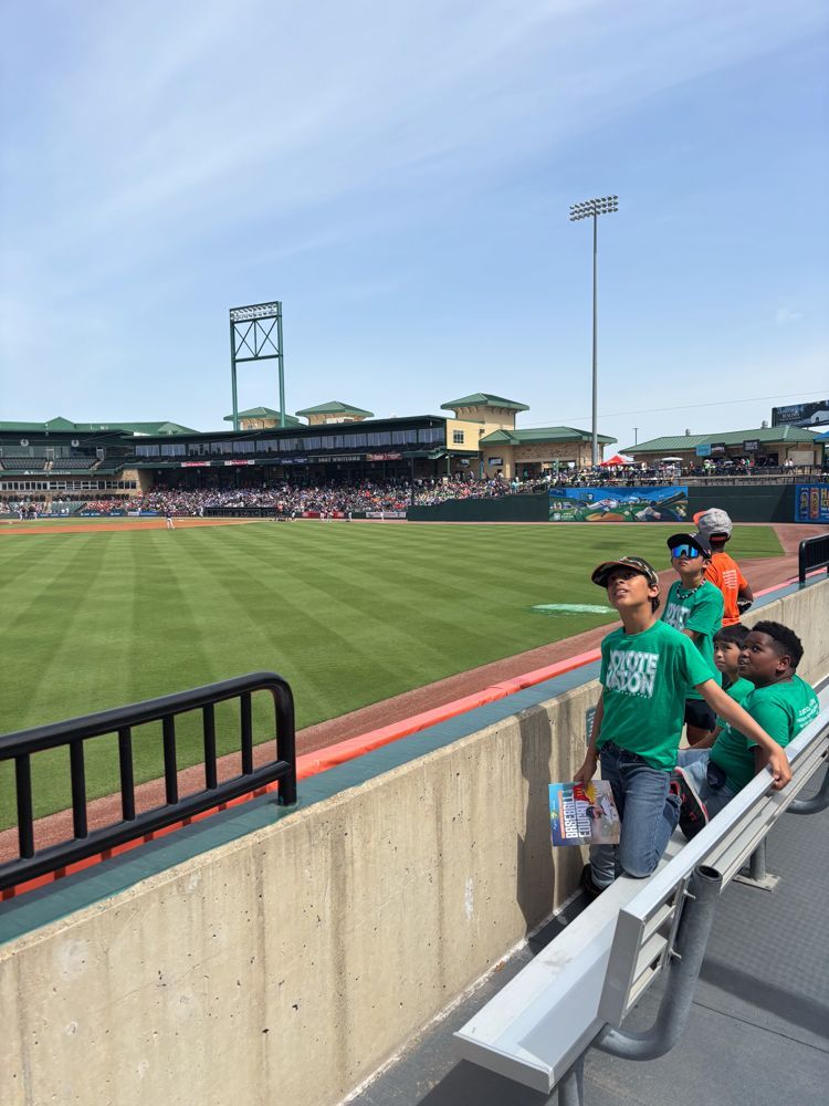 A group of children are sitting in the stands at a baseball game.