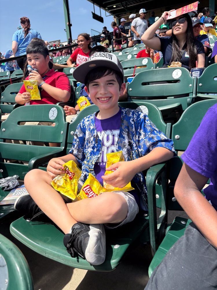 A young boy is sitting in a stadium eating chips.