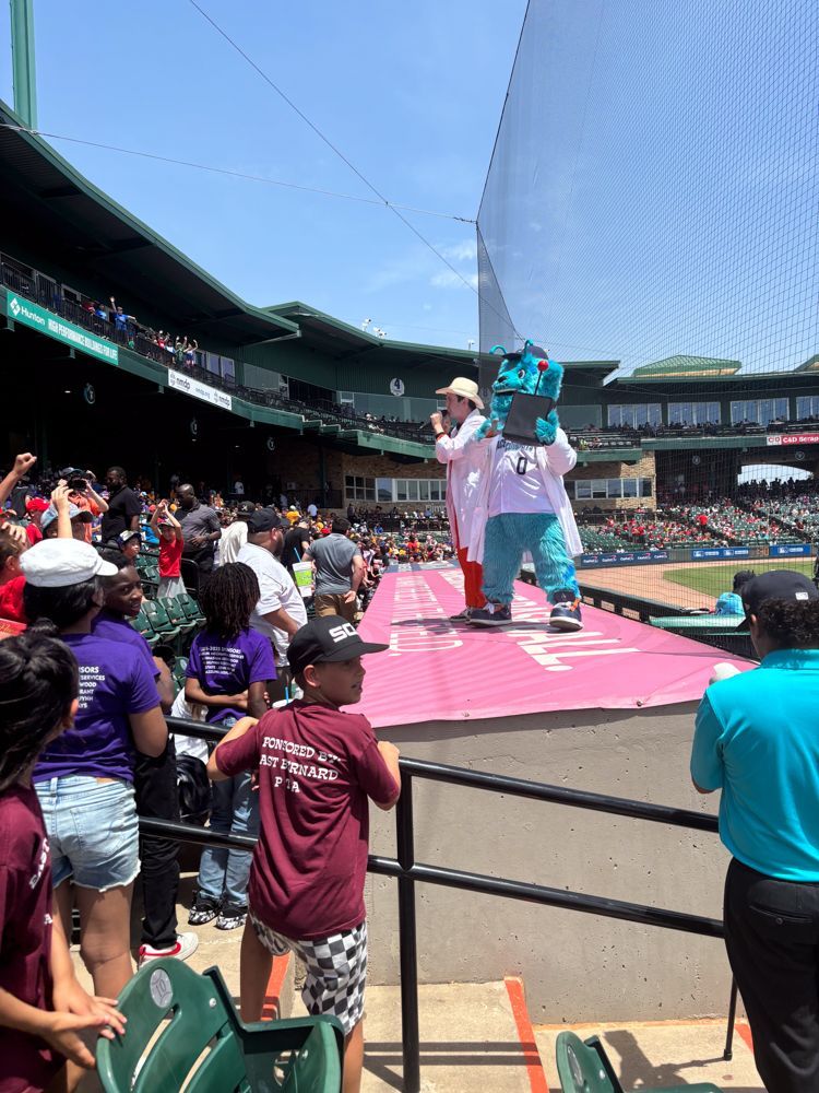 A mascot is standing on a stage in front of a crowd at a baseball game.