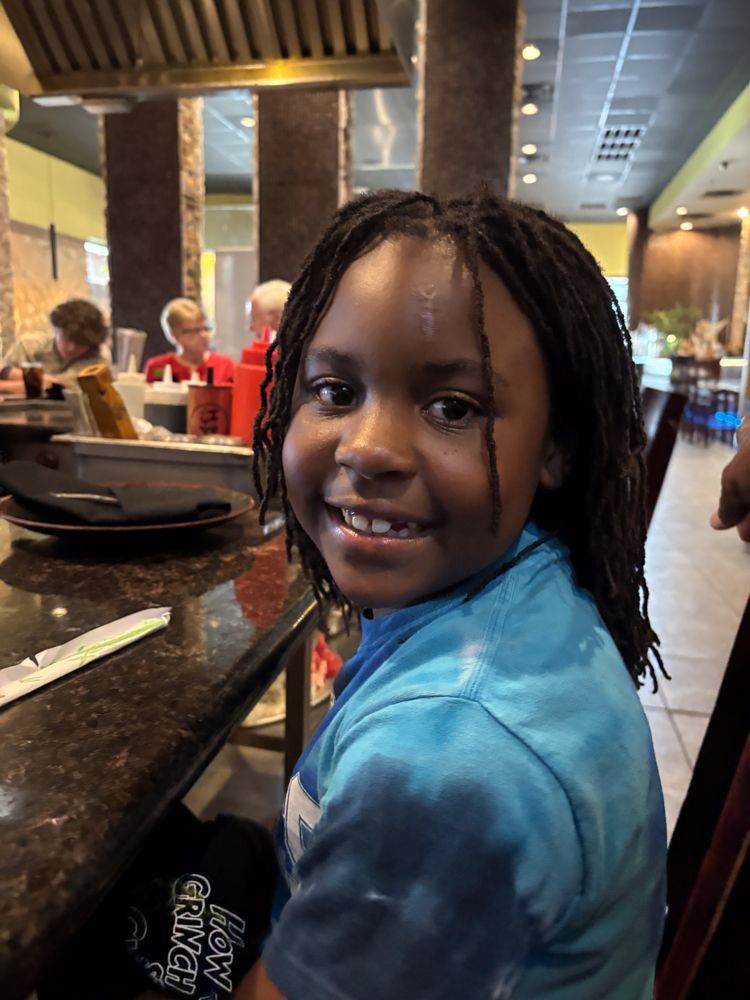 A young boy with dreadlocks is sitting at a table in a restaurant.
