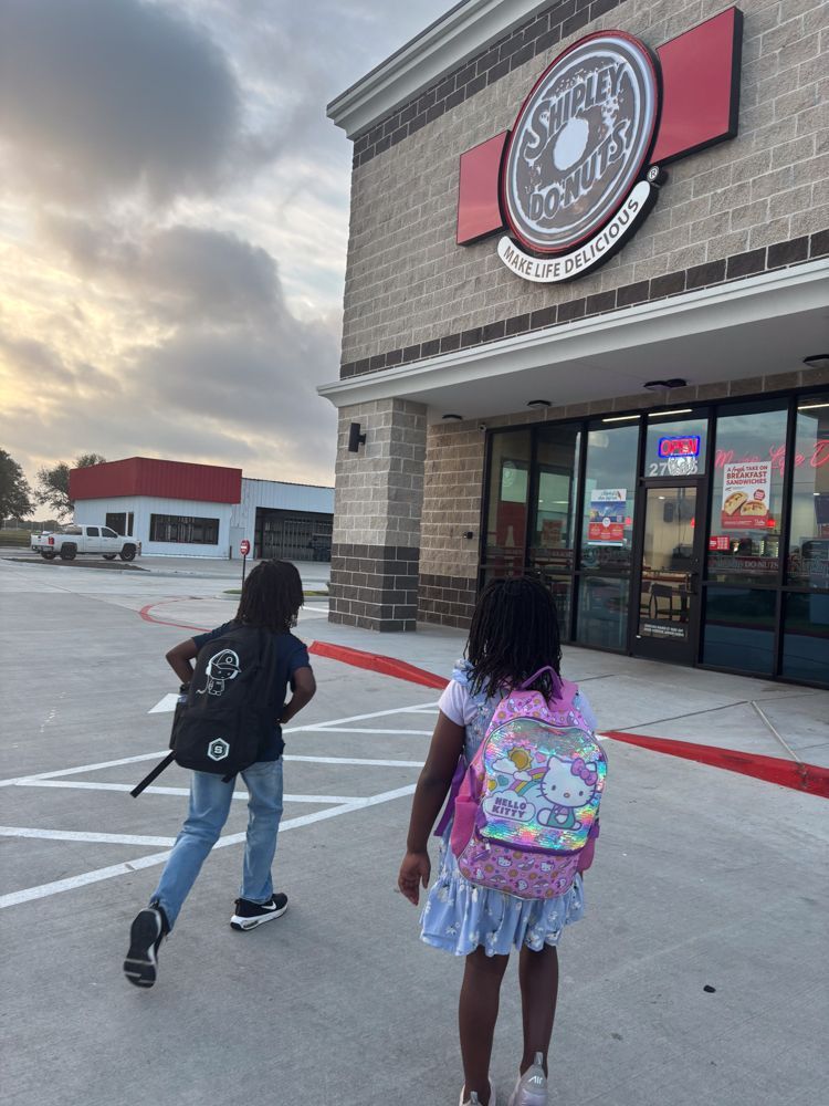 A boy and a girl are walking towards a donut shop.
