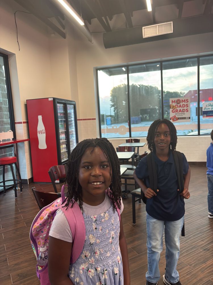A girl with a backpack is standing next to a boy in a restaurant.