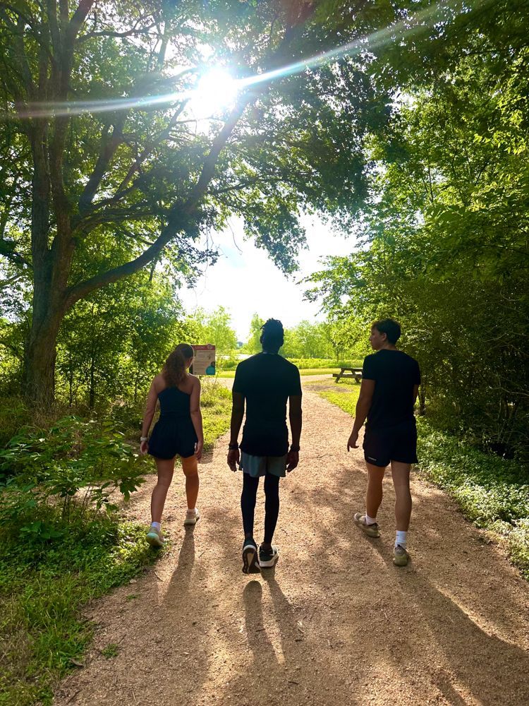 Three people are walking down a dirt path in the woods.