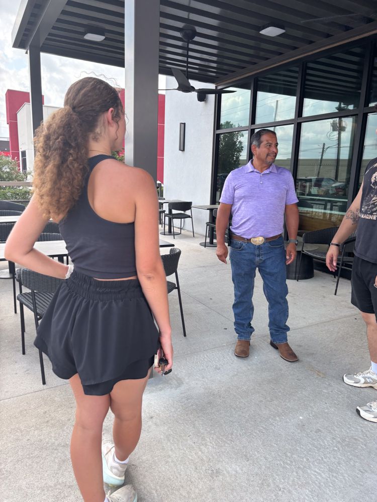 A man and a woman are standing outside of a restaurant talking to each other.
