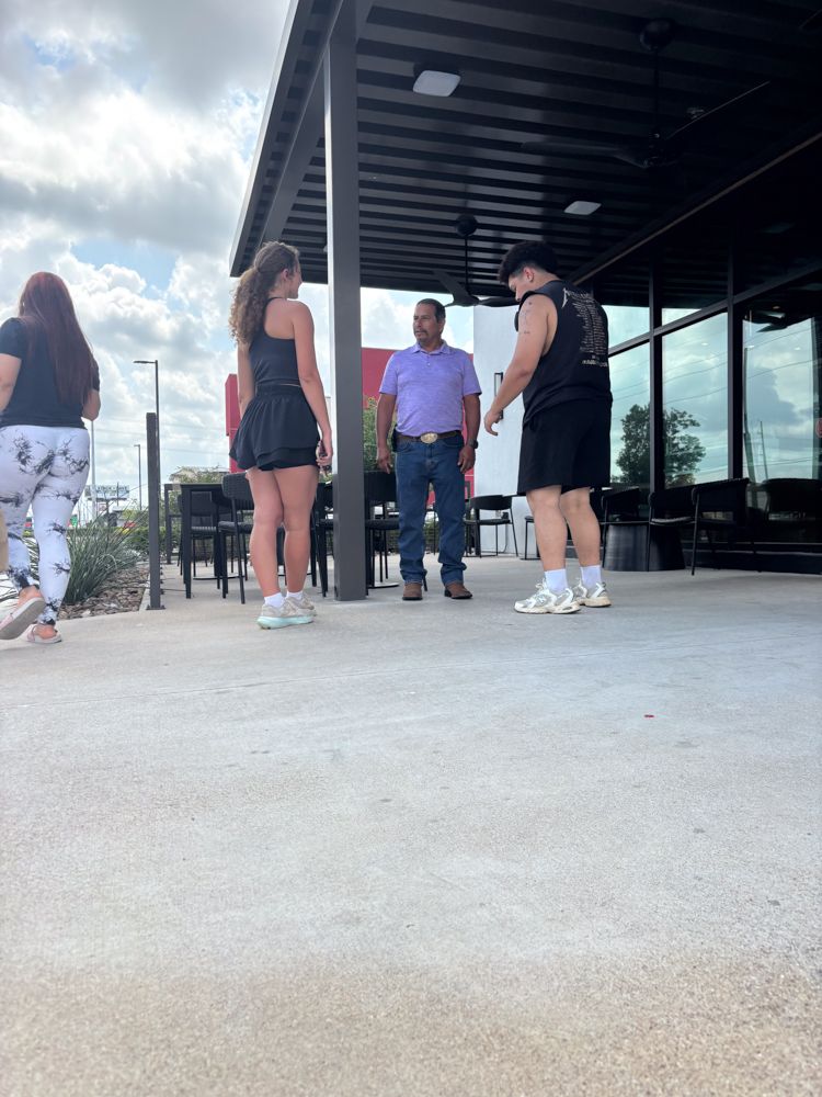 A group of people are standing on a sidewalk in front of a building.