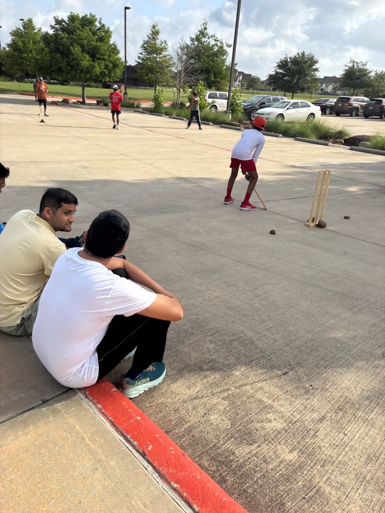 A group of young men are playing a game of cricket in a parking lot.