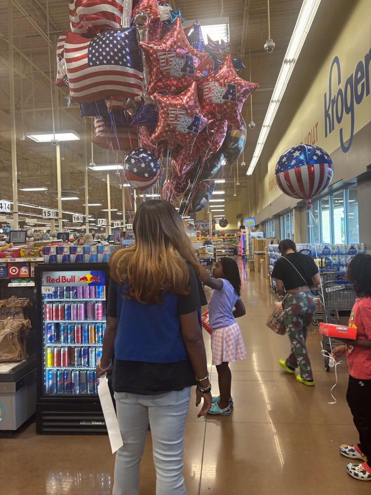 A woman holding a child in a grocery store with balloons hanging from the ceiling