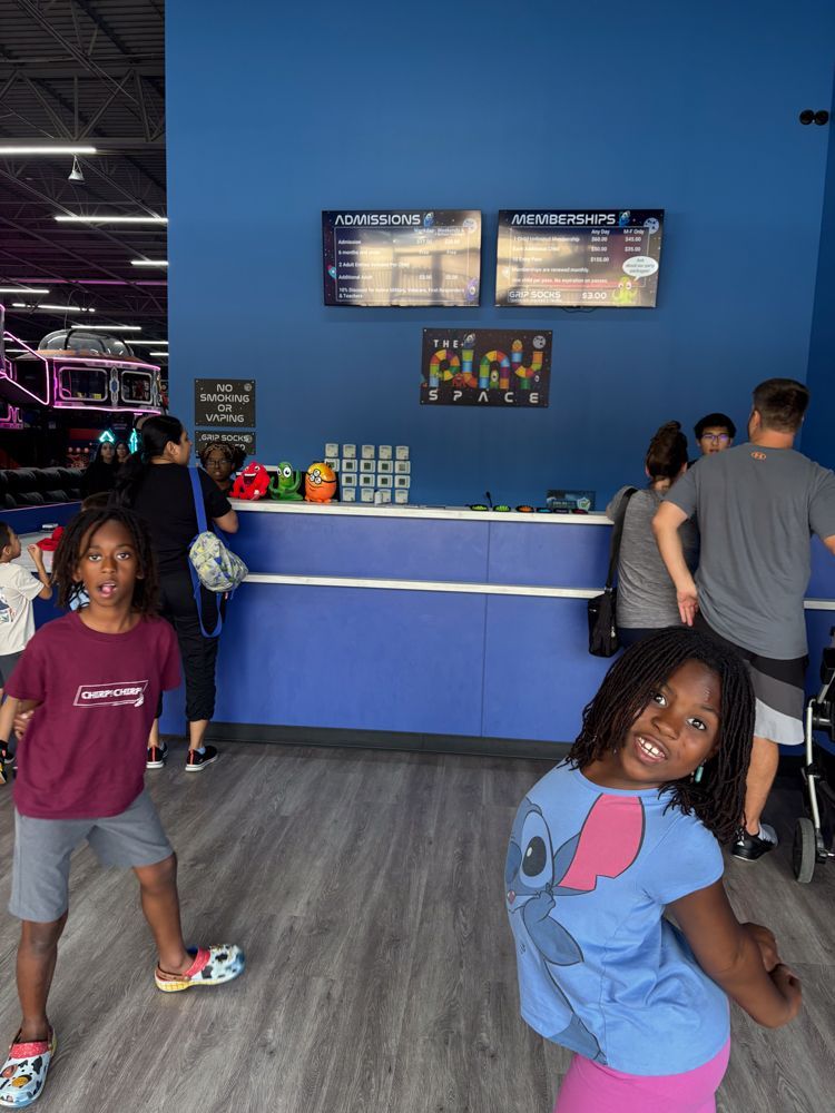 A girl in a stitch shirt is standing in front of a counter in a store.