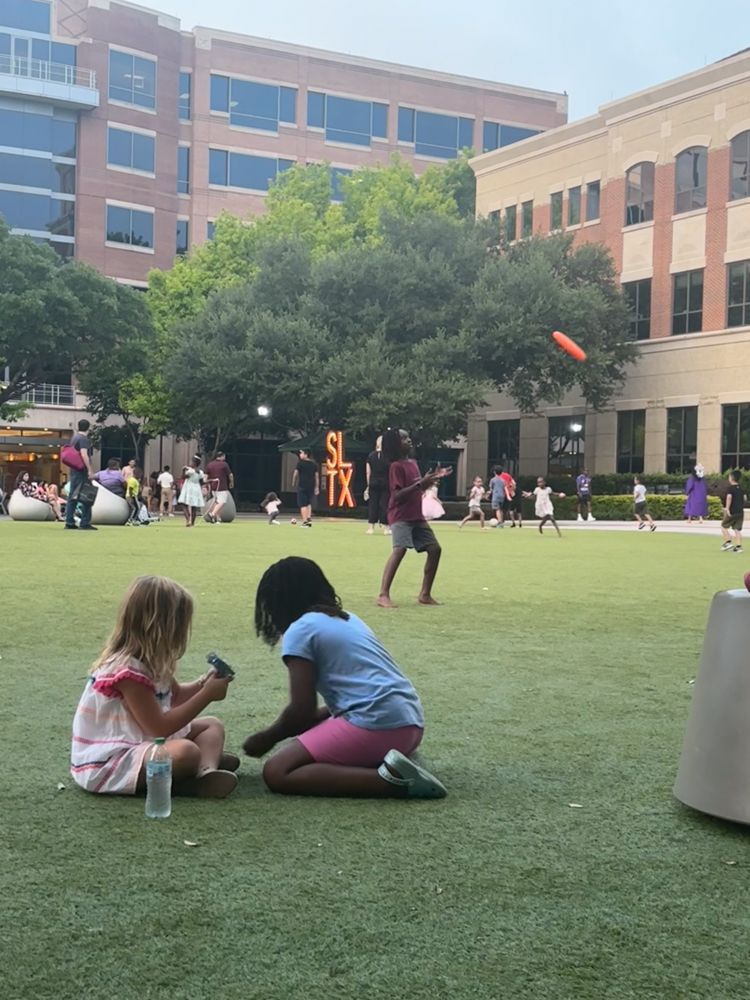 Two little girls are sitting on the grass playing with a frisbee