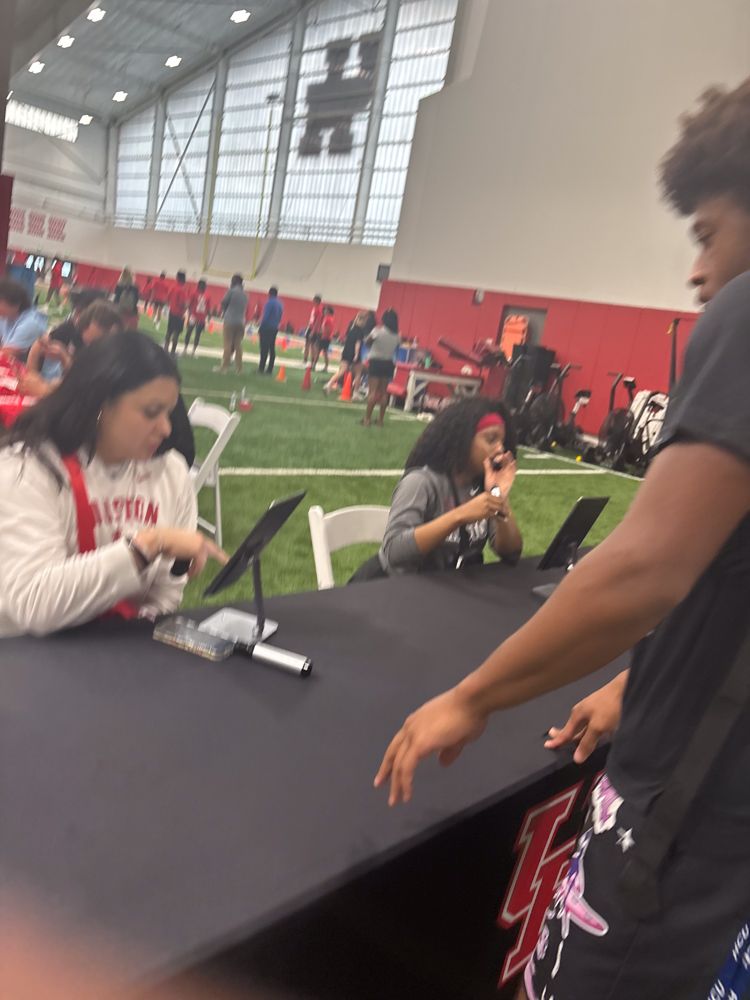 A group of people are sitting at a table with a large h on the wall behind them