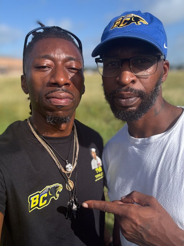 Two men are posing for a picture and one of them is wearing a blue hat.