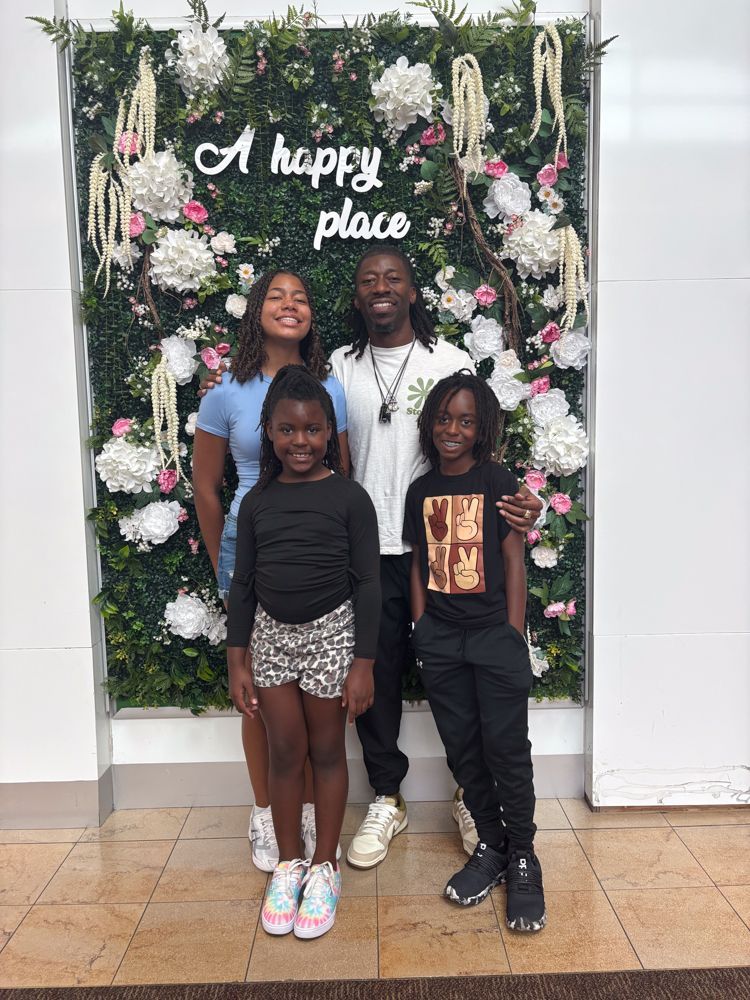 A family is posing for a picture in front of a wall of flowers.