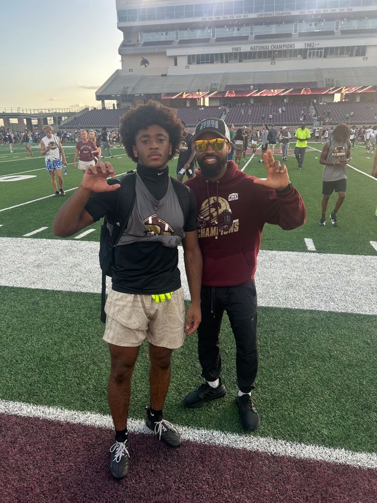 Two men are standing next to each other on a football field.