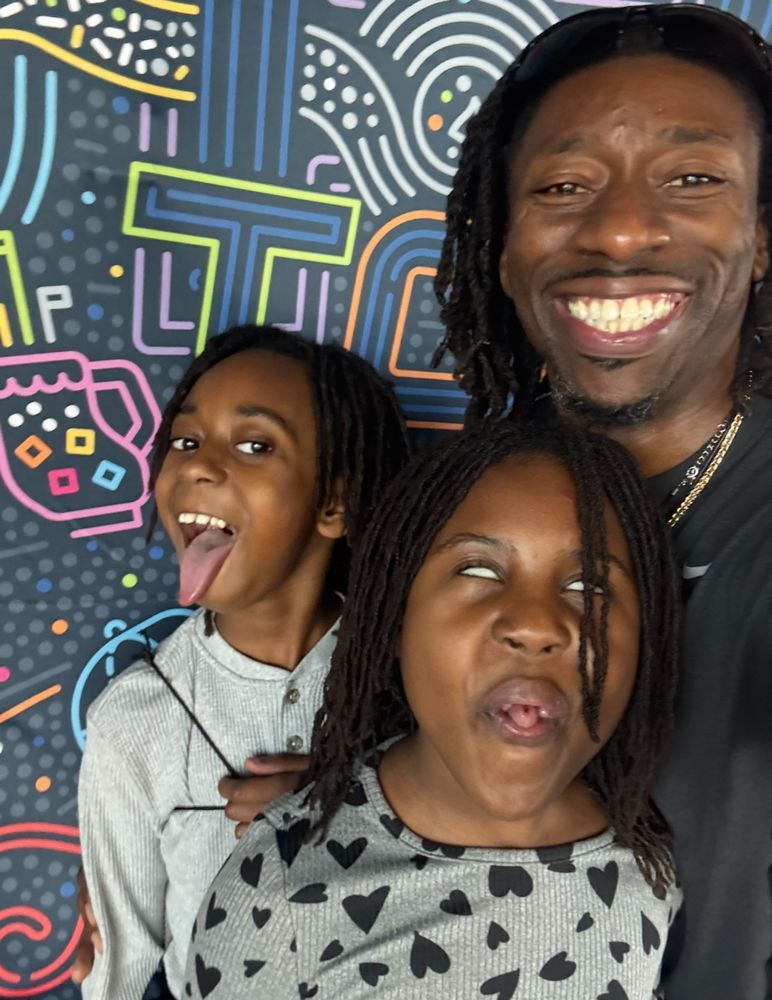 A man and two children are making funny faces in front of a colorful wall