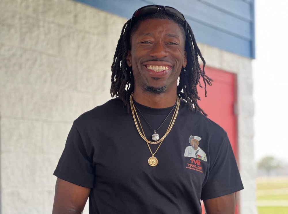 A man with dreadlocks is wearing a black t-shirt and gold necklaces.