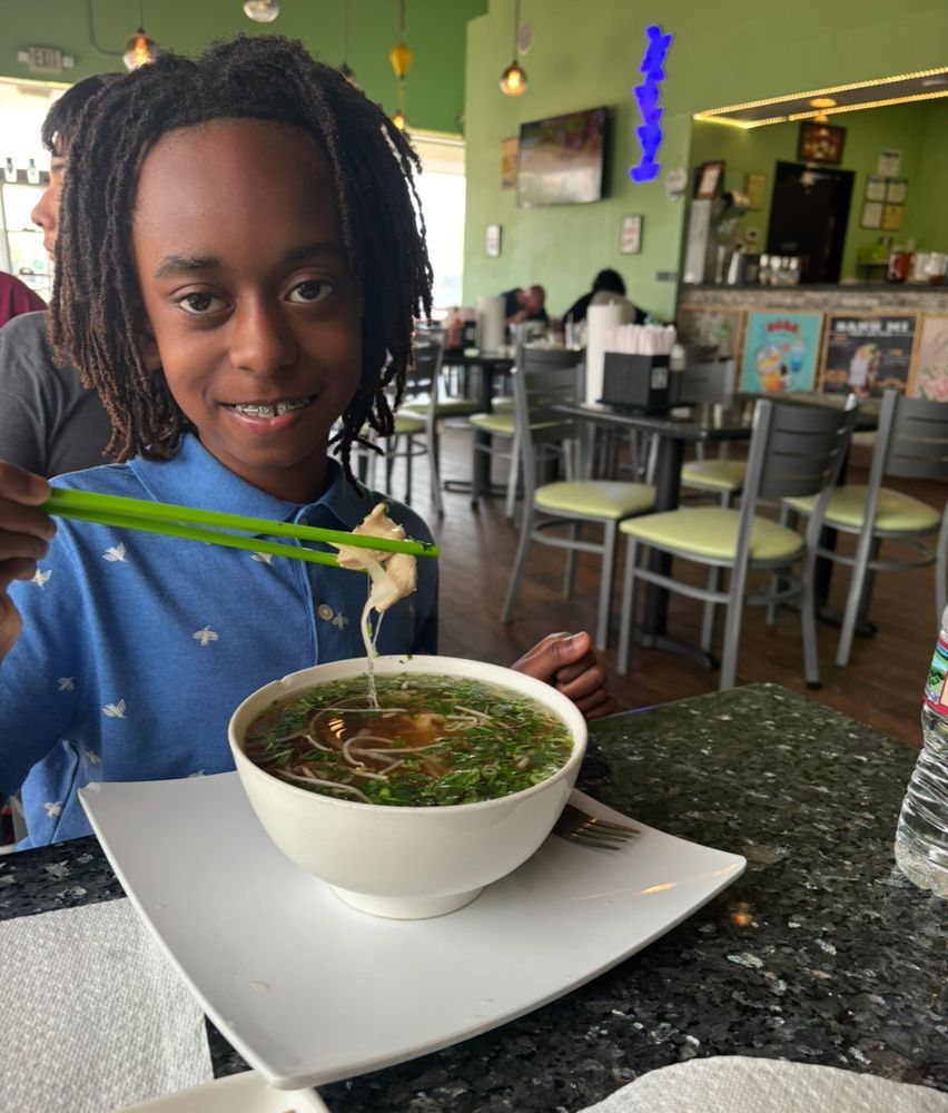 A young boy is eating a bowl of soup with chopsticks