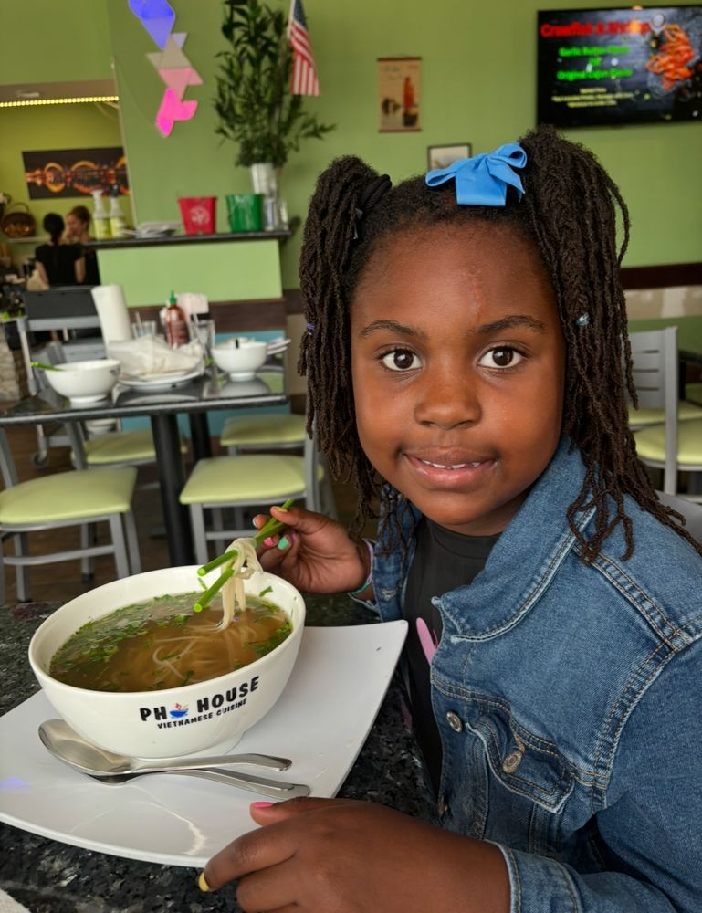A little girl is eating a bowl of soup in a restaurant