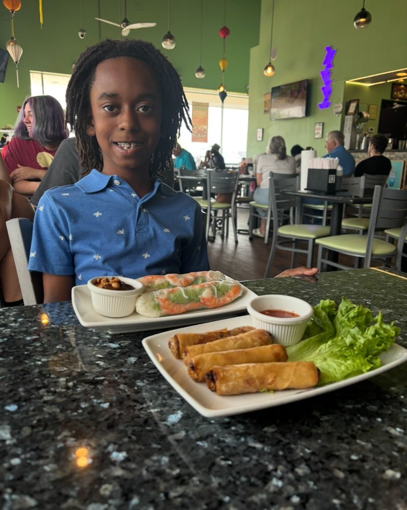 A young boy is sitting at a table with plates of food.