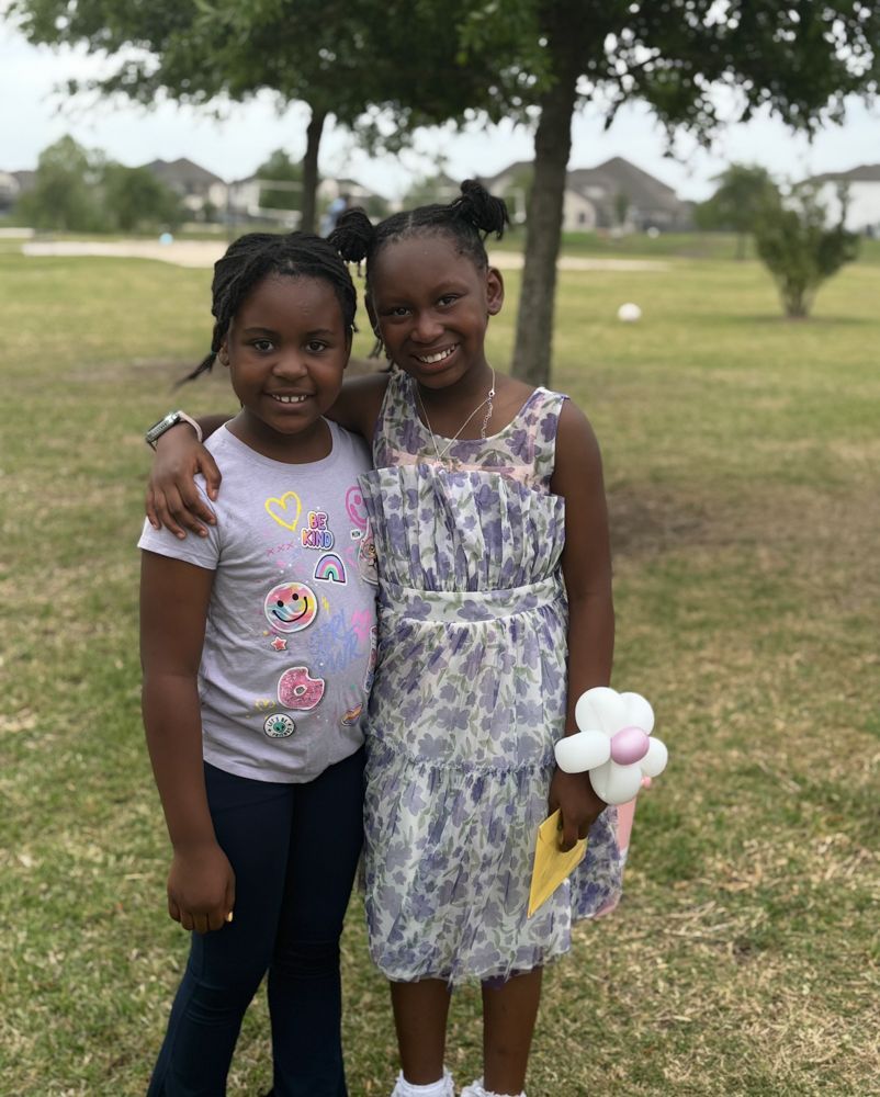 Two young girls are posing for a picture in a park.