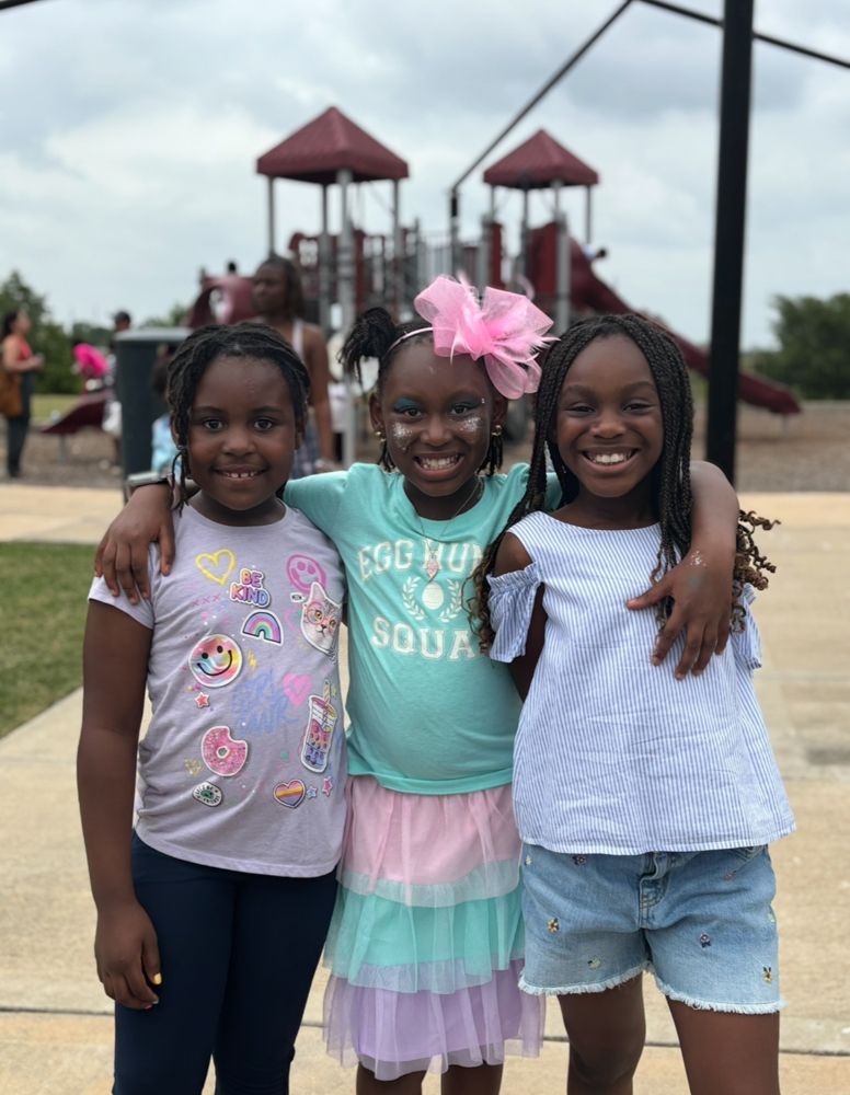 Three young girls are posing for a picture in front of a playground.
