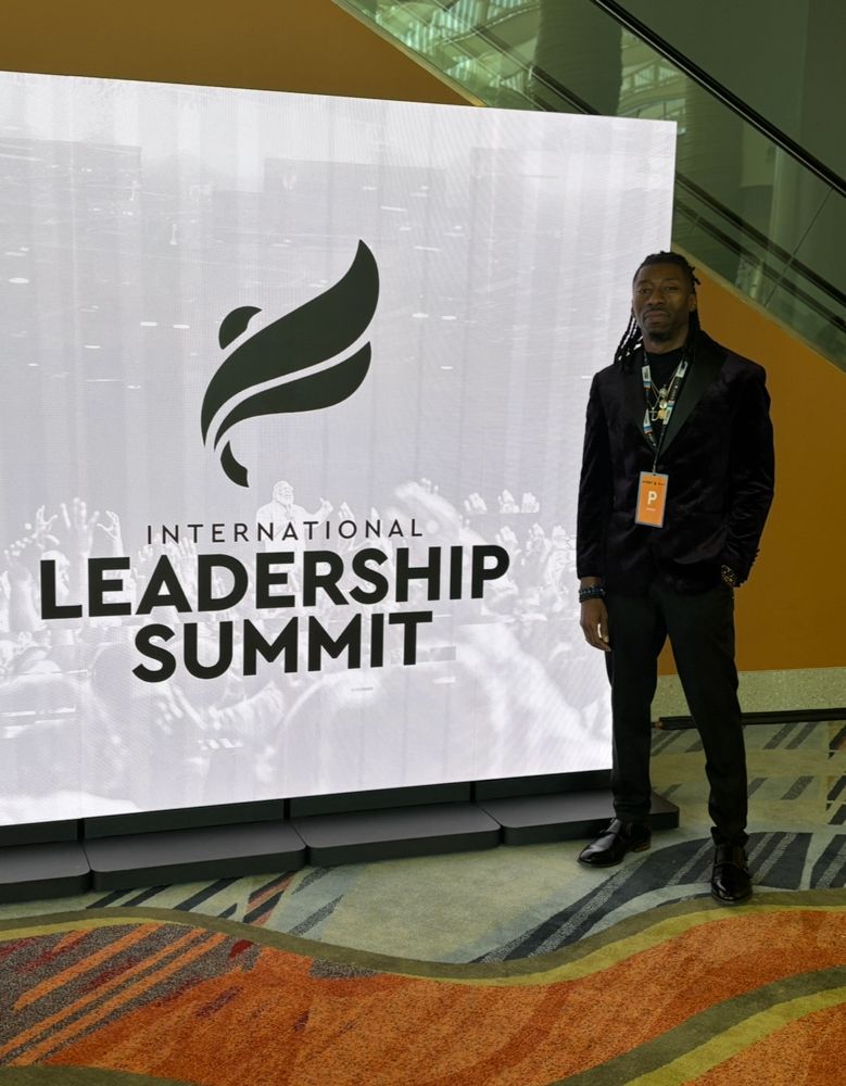 A man is standing in front of a sign that says international leadership summit