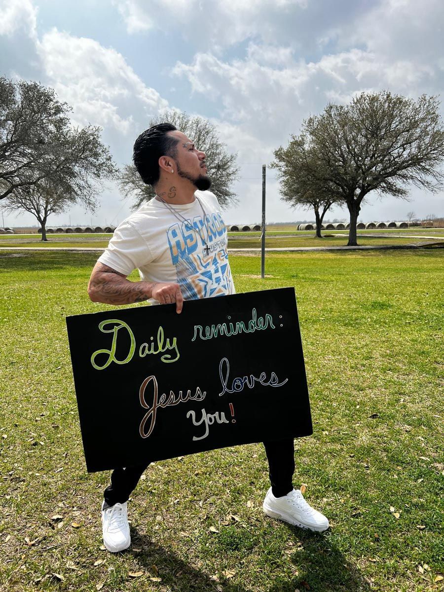 A man is holding a sign that says daily reminder jesus loves you.