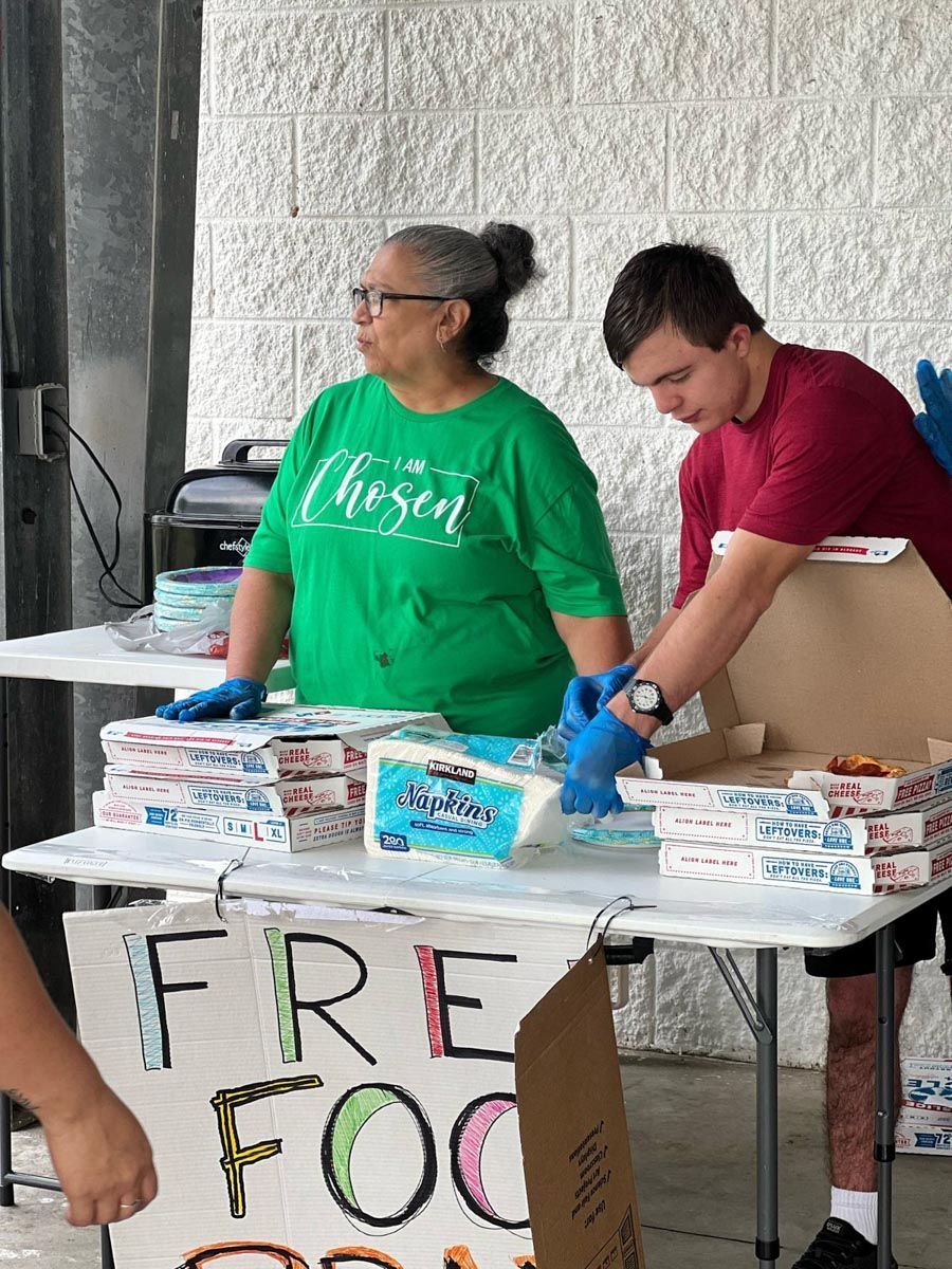 A man and a woman are standing at a table with boxes of food.