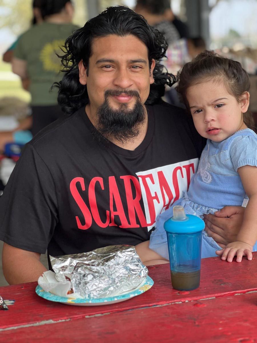 A man wearing a scarface shirt holds a little girl