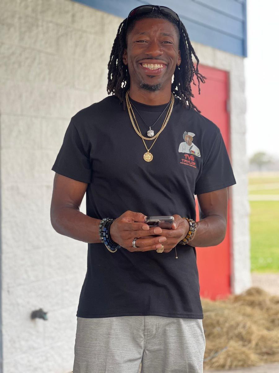 A man wearing a black t-shirt is smiling and holding a cell phone