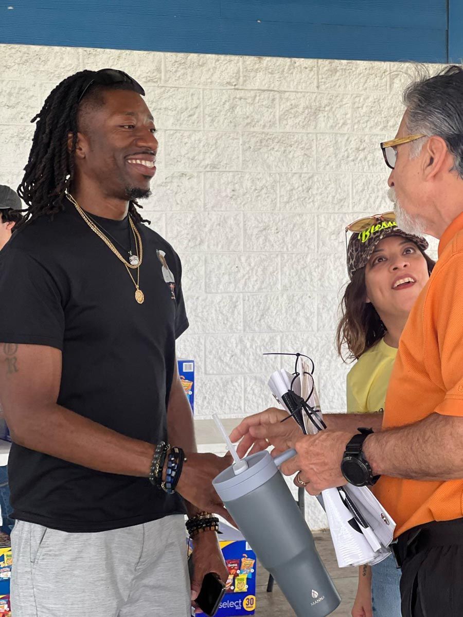 A man in a black shirt is talking to a man in an orange shirt