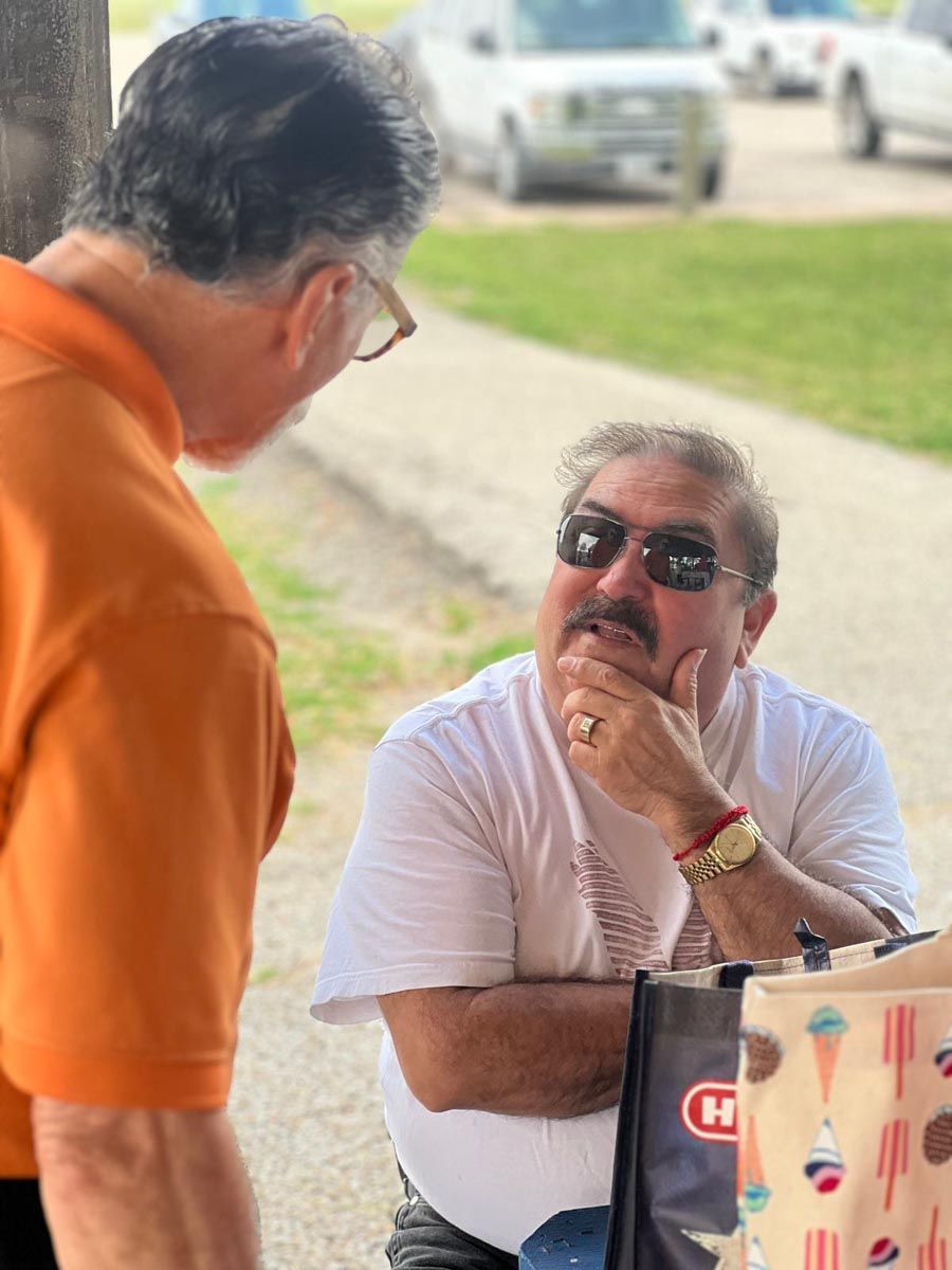 A man wearing sunglasses is talking to another man