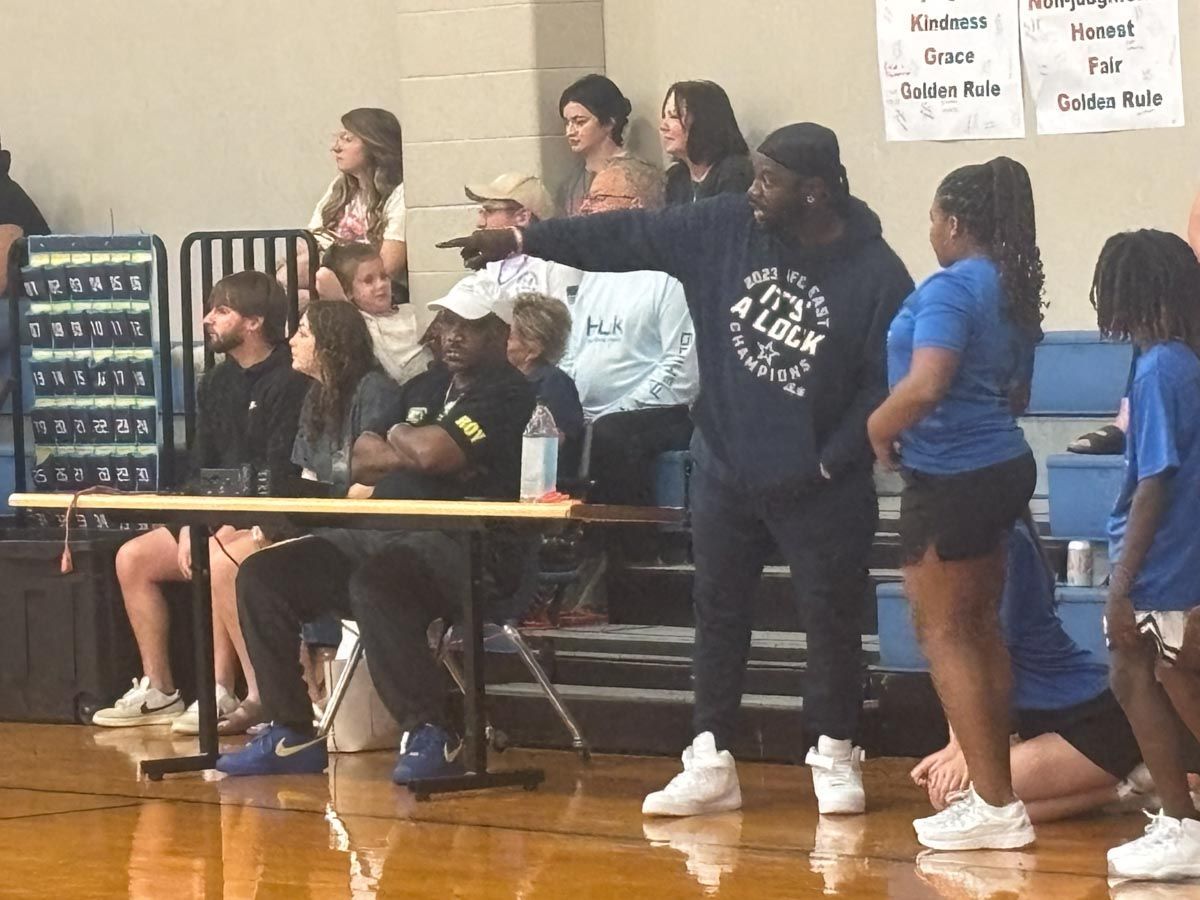 A group of people are watching a basketball game and one of them is wearing a shirt that says alex