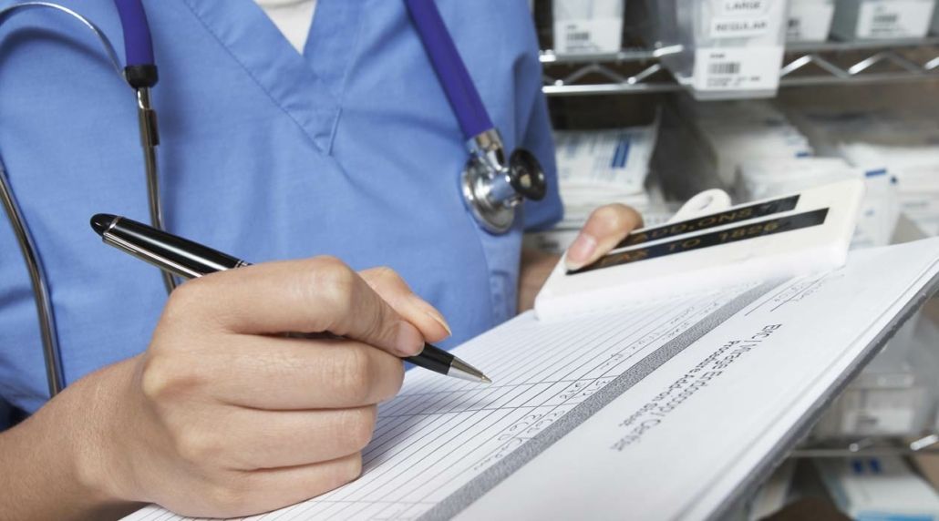 A doctor is writing on a clipboard with a pen.