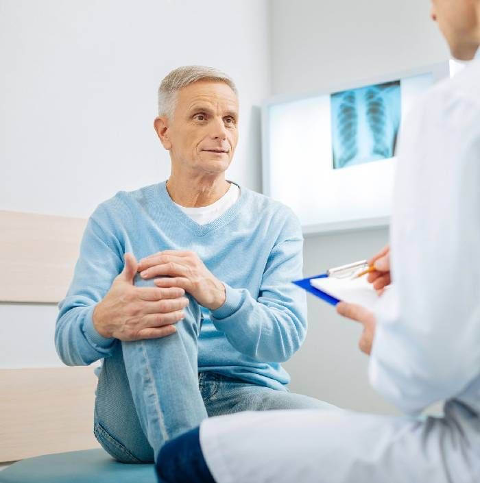 Good Looking Nice Aged Man Holding His Knee and Looking at His Doctor