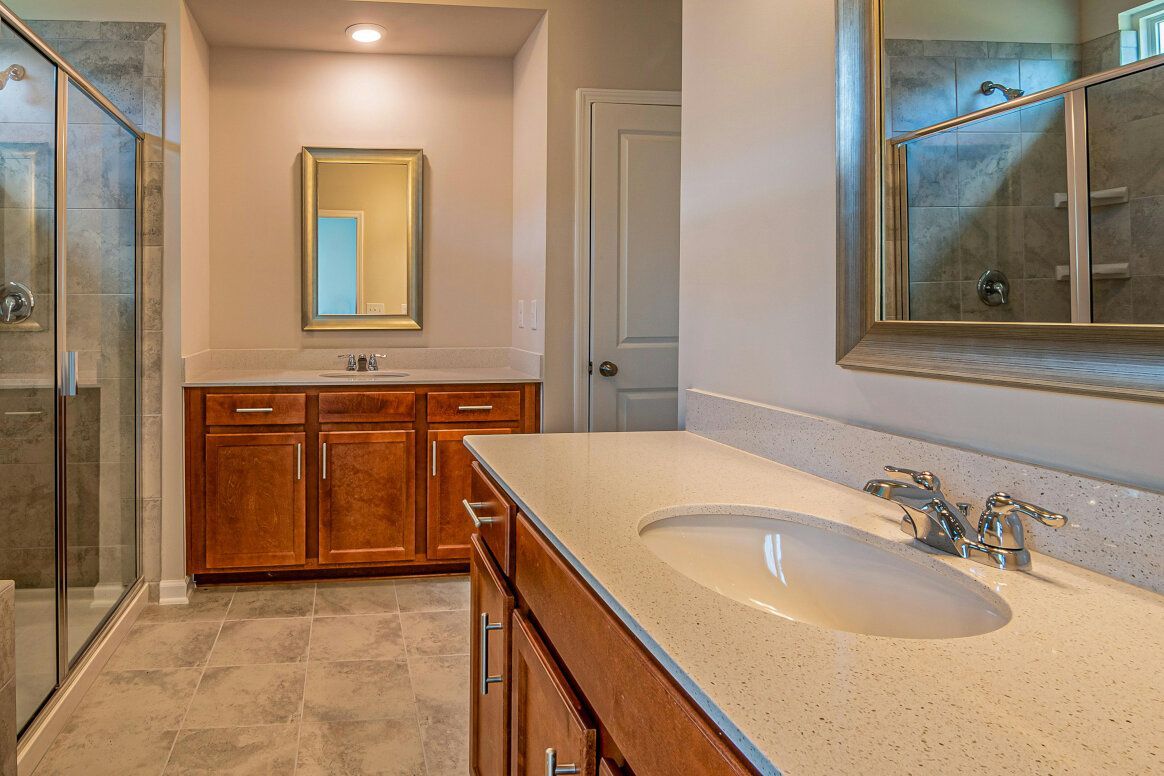 Bathroom with a vanity, sink, and walk-in shower. Brown cabinets, neutral-colored countertops, and tiled floors.