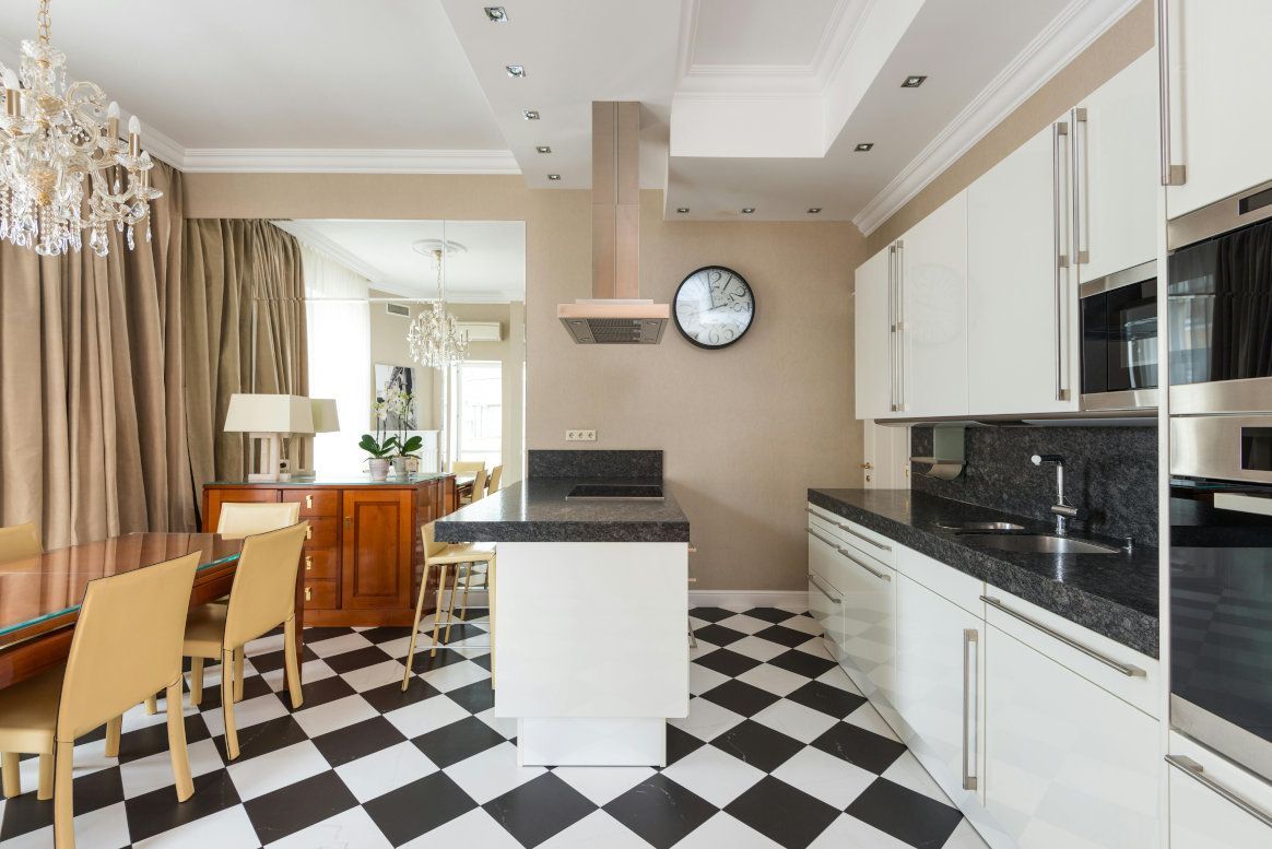 Kitchen with white cabinets, black countertop, checkered floor, and dining area.