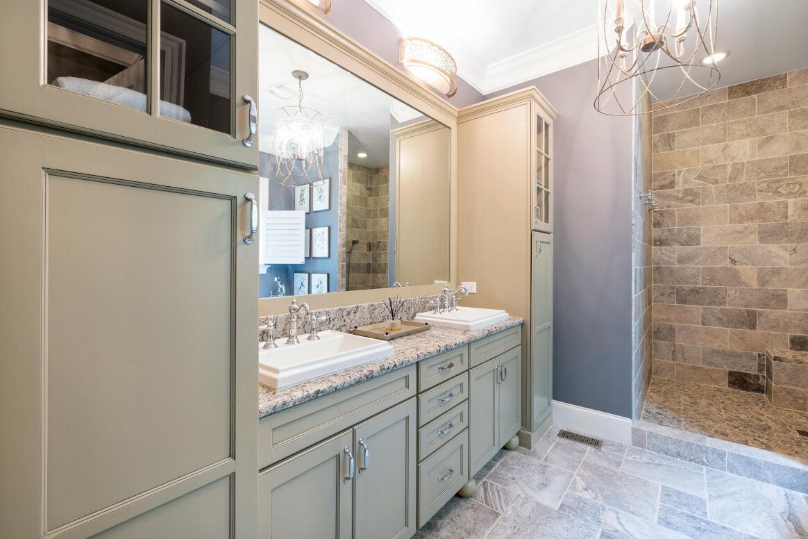 Bathroom with light green cabinets, marble countertop, and stone shower.