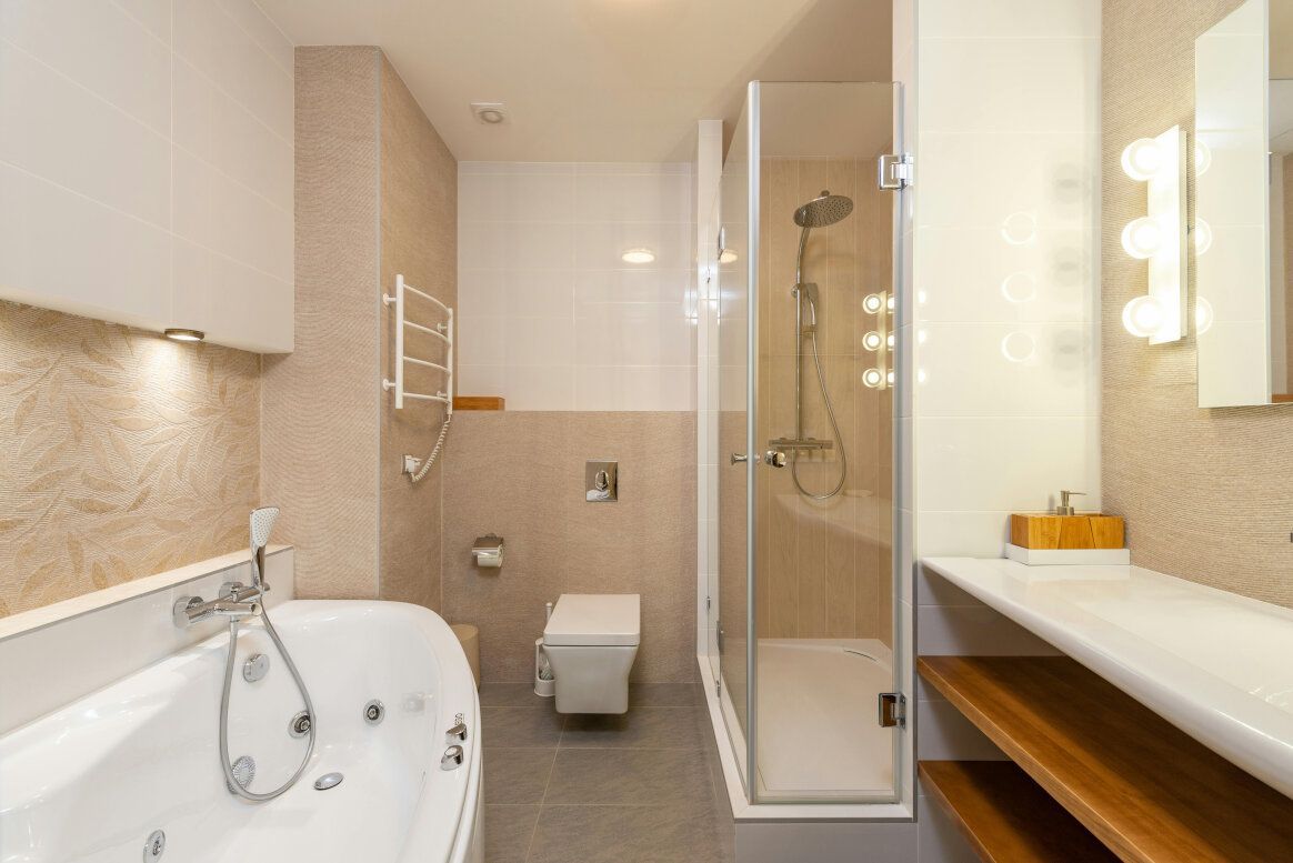 Modern bathroom with a bathtub, shower, toilet, and sink, featuring beige and white tones.
