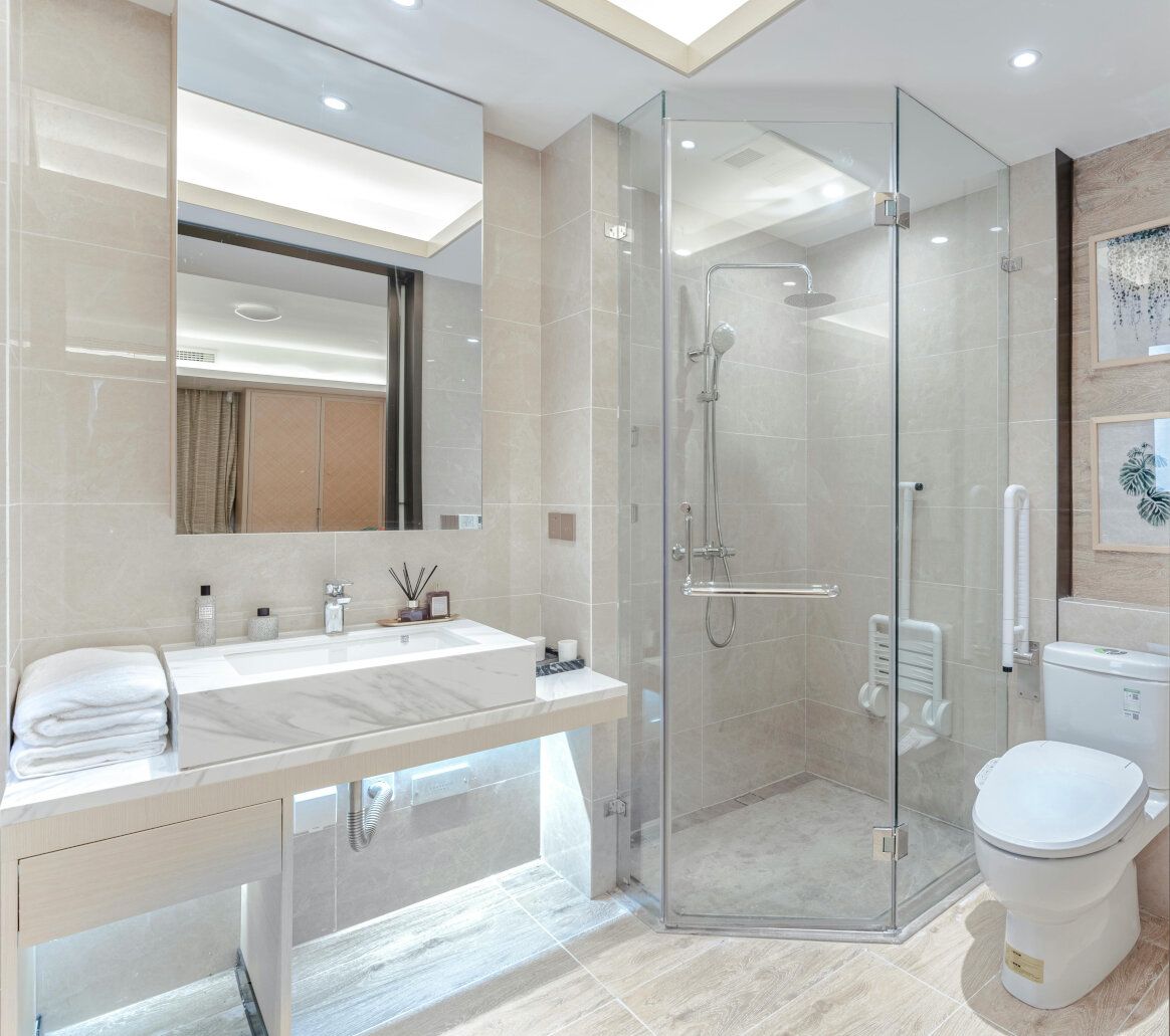 Modern bathroom with glass shower, white sink, and toilet; light-colored tile walls.
