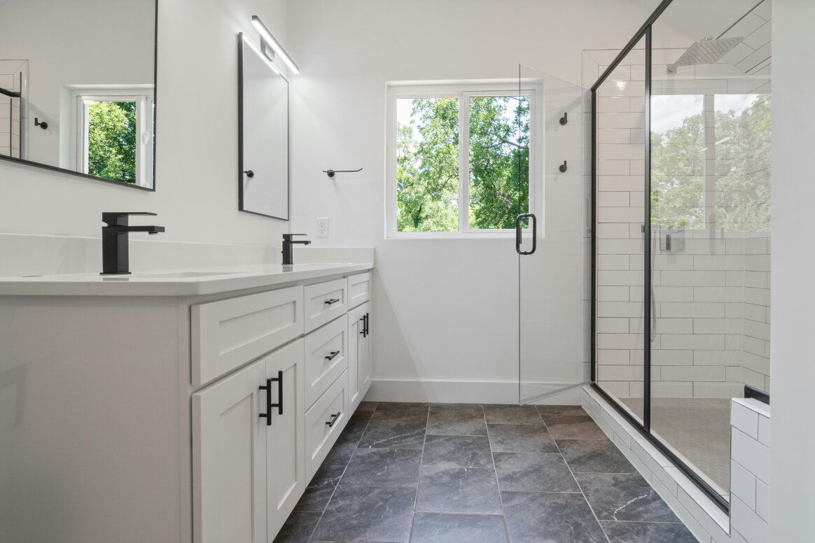 Modern white bathroom with double vanity, black accents, and a glass shower.