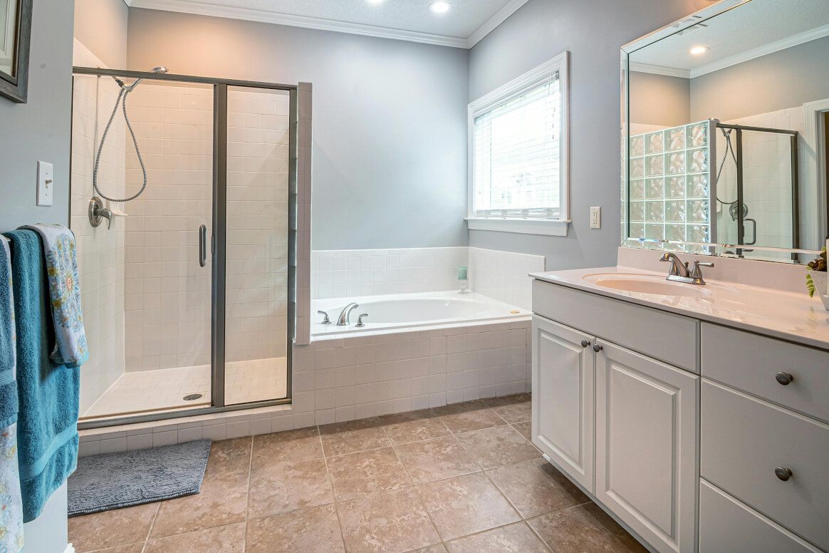 Bathroom with shower, tub, vanity, light gray walls, window, and marble floor.