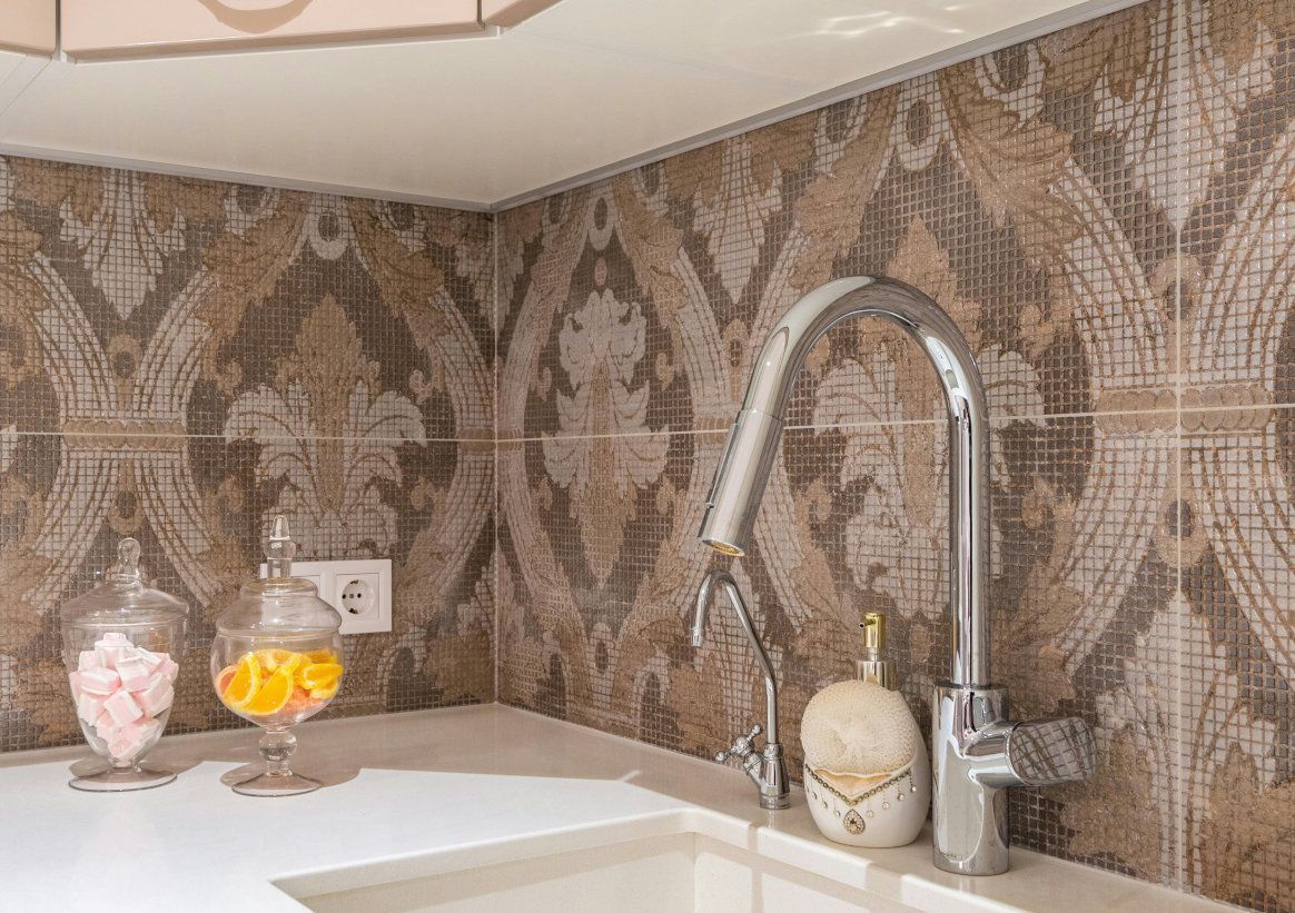 Kitchen with ornate backsplash, white countertop, and chrome faucet.