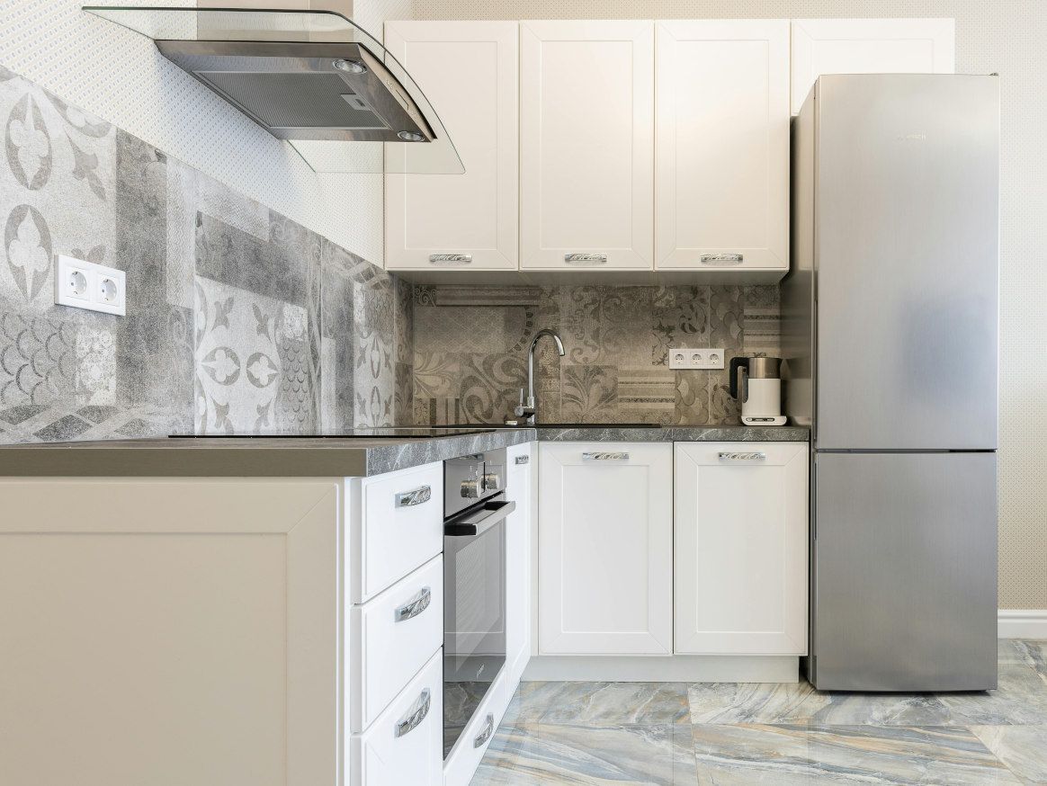 Modern white kitchen with stainless steel appliances and patterned tile backsplash.