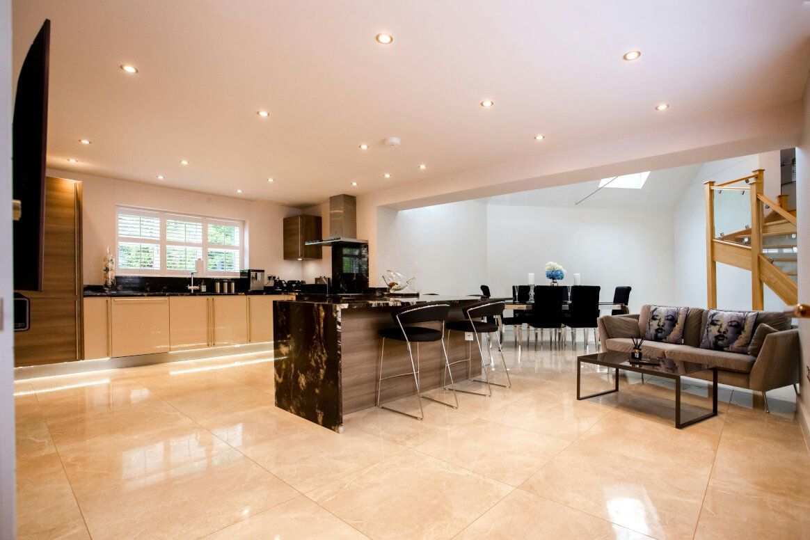 Spacious modern kitchen with island, seating, and dining area. Neutral colors, recessed lighting, and large windows.