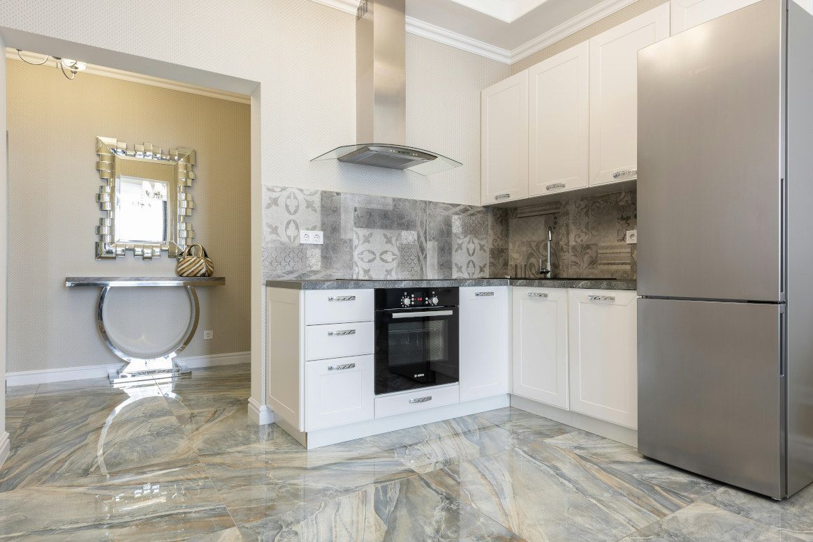 White kitchen with stainless steel appliances, marble floor, and a mirrored entryway.