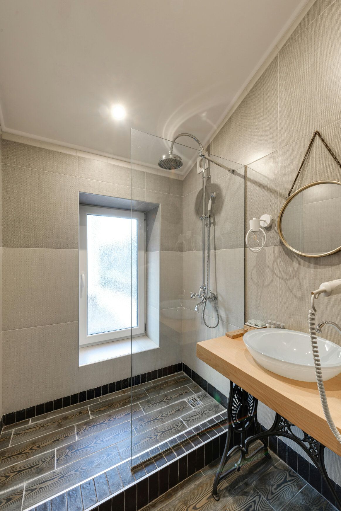 Bathroom with shower, window, sink, and mirror; gray tile walls, wood floor, and wooden countertop.